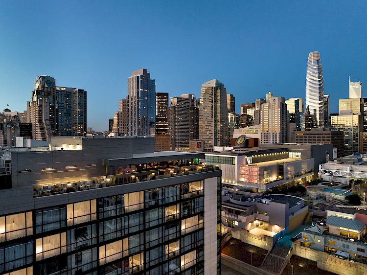 The image shows a city skyline at dusk with high-rise buildings and illuminated windows.