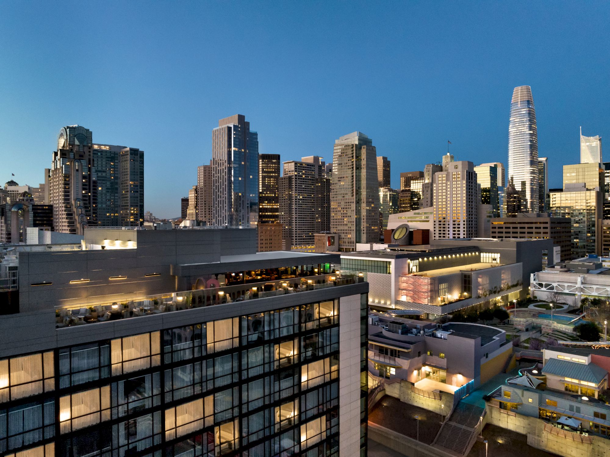 The image shows a city skyline at dusk with high-rise buildings and illuminated windows.