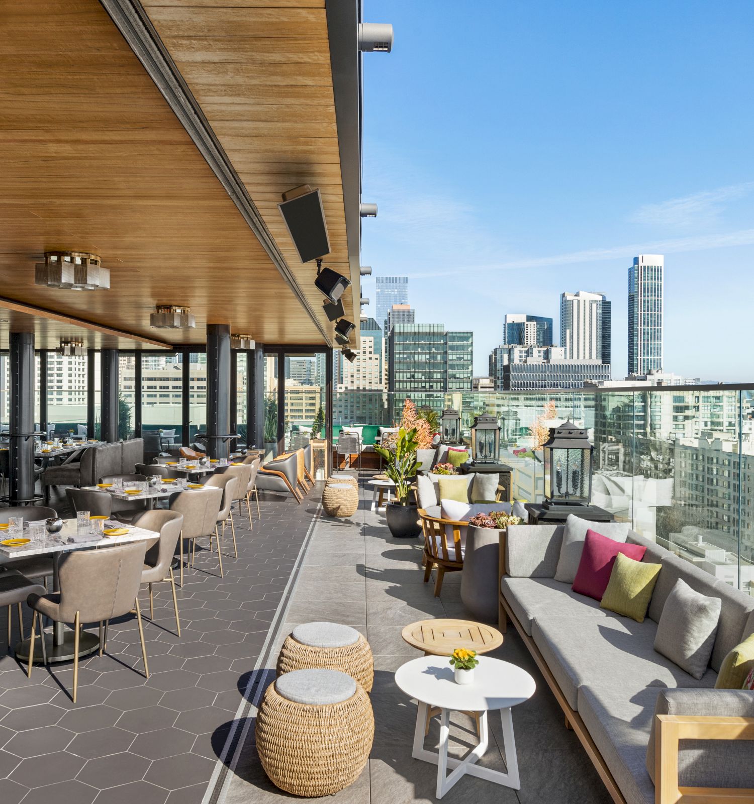 A rooftop bar with city views featuring modern seating, tables set for dining, and a mix of indoor-outdoor areas with stylish decor.