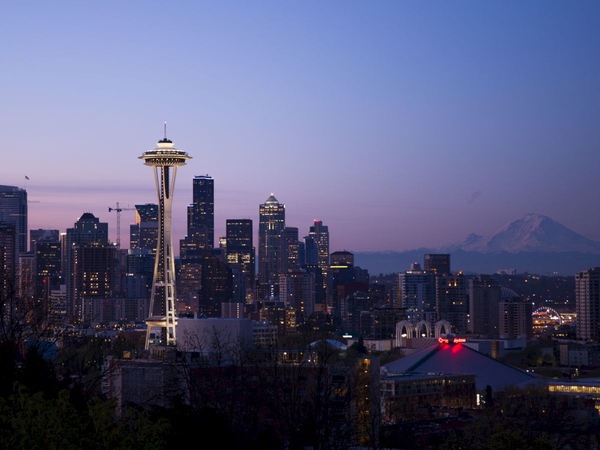 The image depicts Seattle's skyline at twilight, featuring the illuminated Space Needle, various buildings, and Mount Rainier in the background.