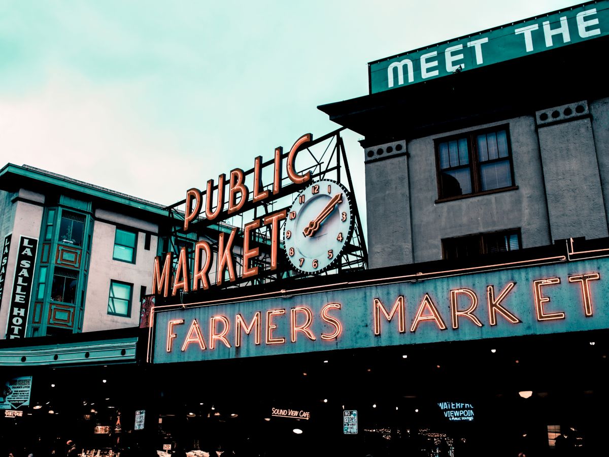 A neon sign reading "Public Market" and "Farmers Market" with a clock on a historic building. The sign promotes a well-known marketplace.