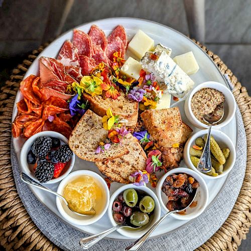 The image shows a charcuterie board with meats, cheeses, bread, olives, nuts, honey, berries, pickles, and mustard arranged in bowls on a platter.