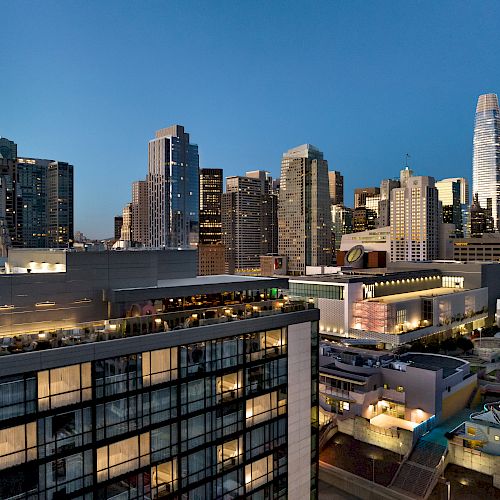 A city skyline during evening with various high-rise buildings and skyscrapers, modern architecture, and illuminated windows.