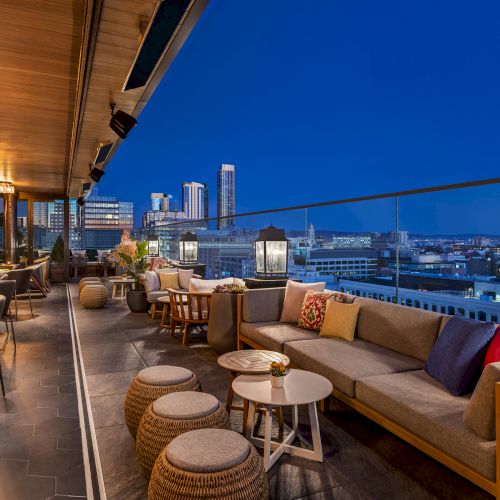 A stylish rooftop lounge at dusk with comfortable seating, lanterns, and city skyline in the background, perfect for sunset cocktails.